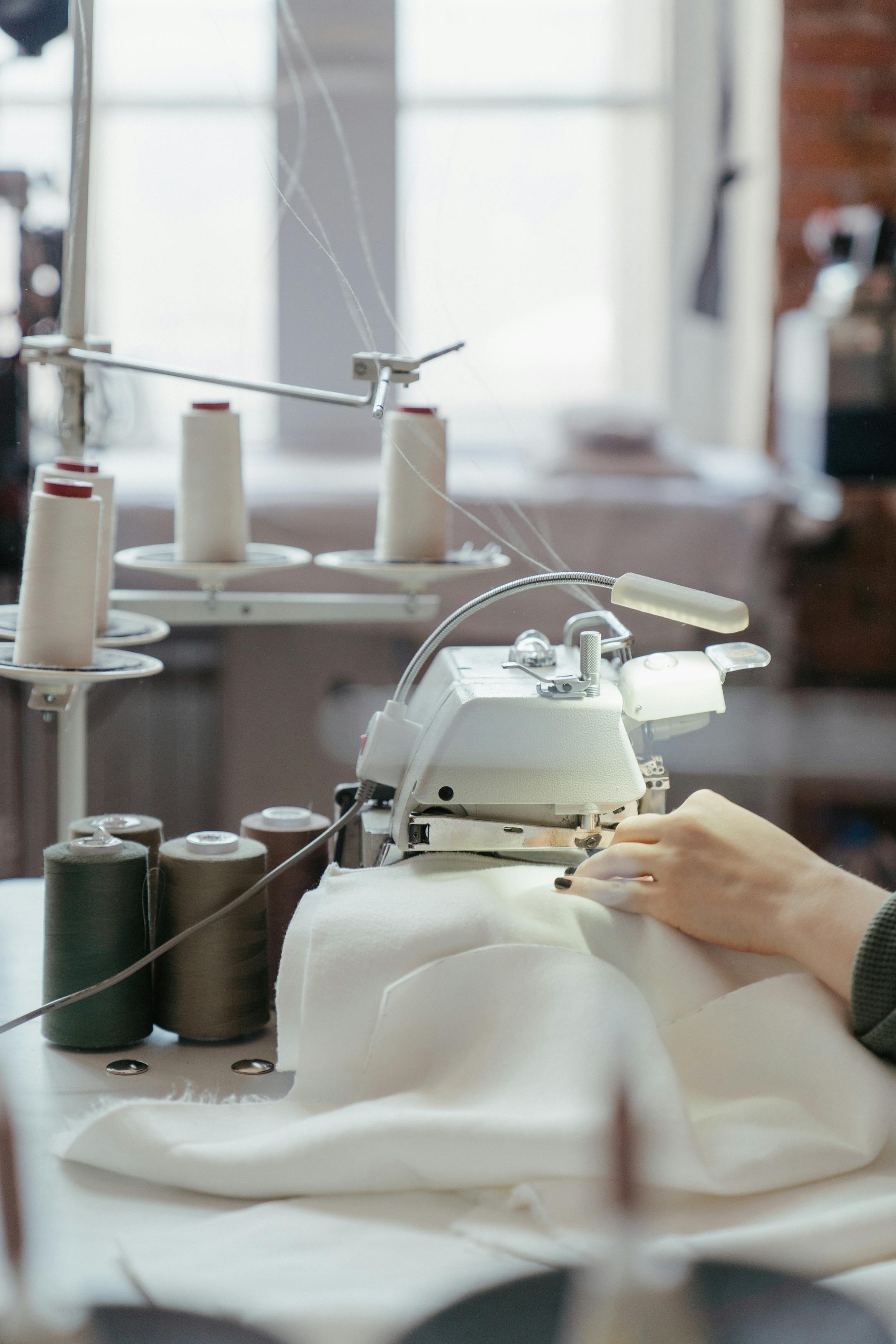pexels-photo-4621910-4621910 A person sewing fabric on a professional machine in a well-lit workshop with spools of thread.